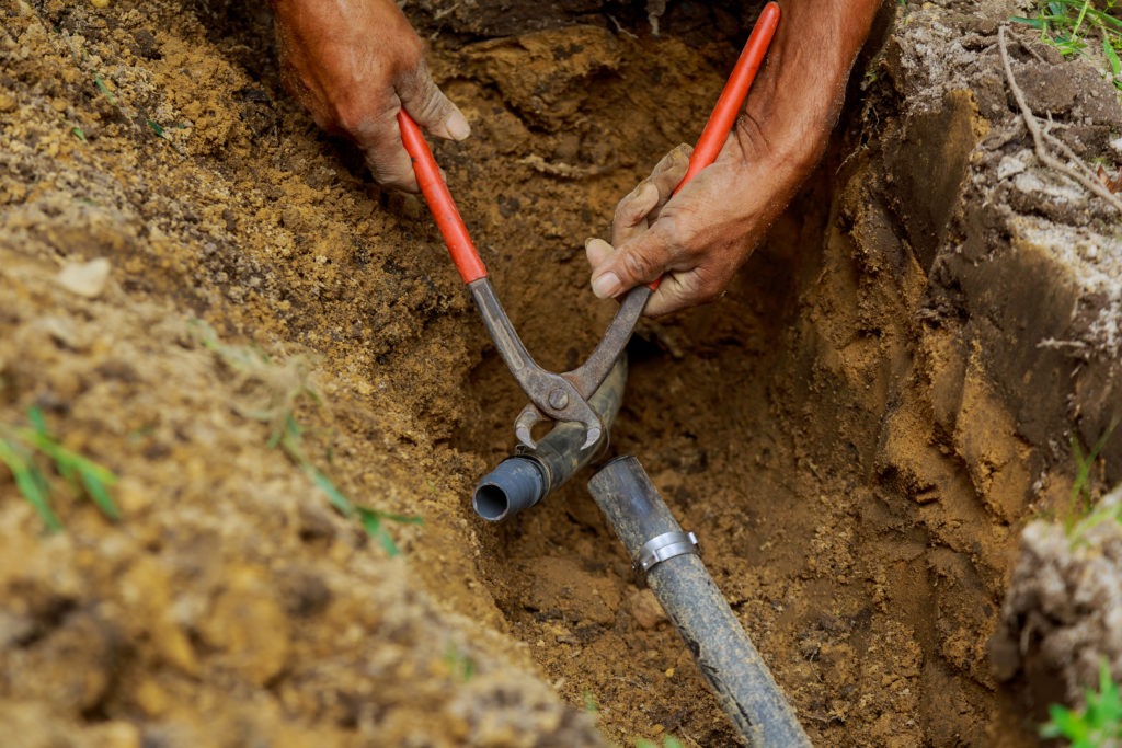 Man Applying Solvent Primer and Cement to PVC Pipes as Part of Installation of Underground